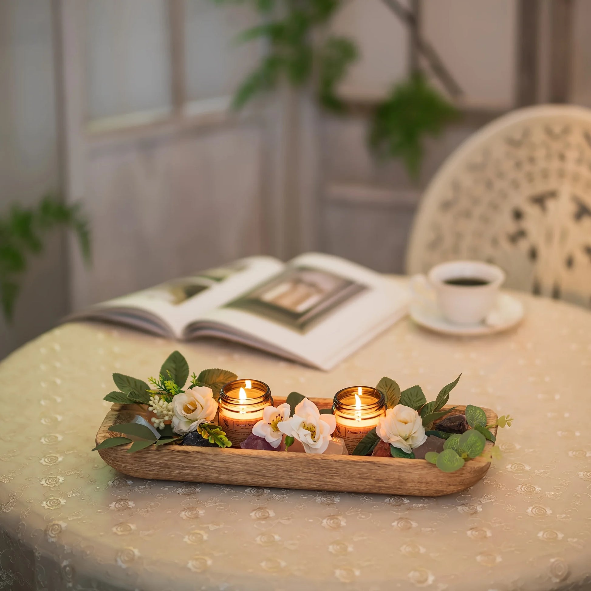 Decorative tray with candles and flowers on a table with a book and cup in the background.