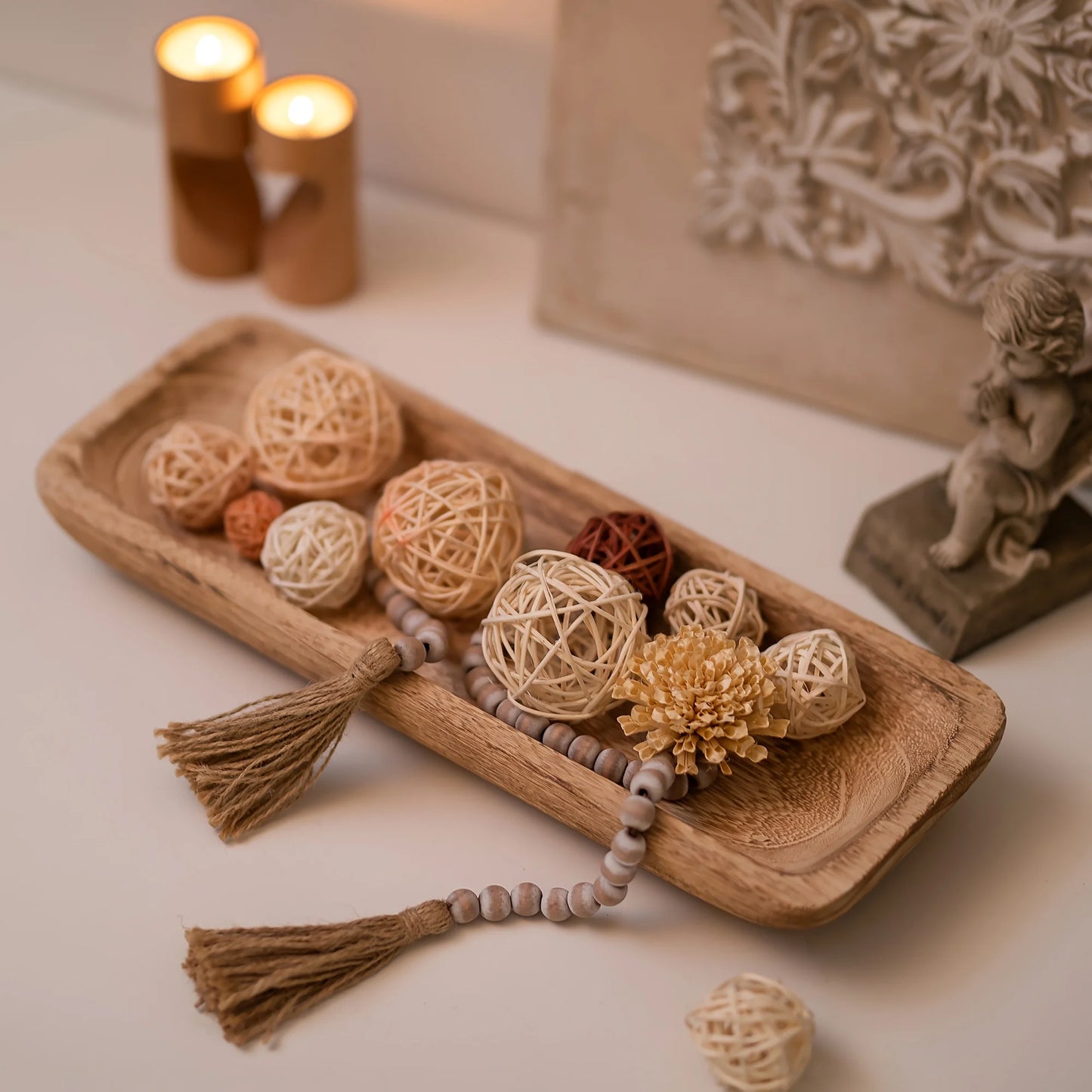 Decorative items including a wooden tray with spherical ornaments and tassels, candles, and a figurine on a neutral background.