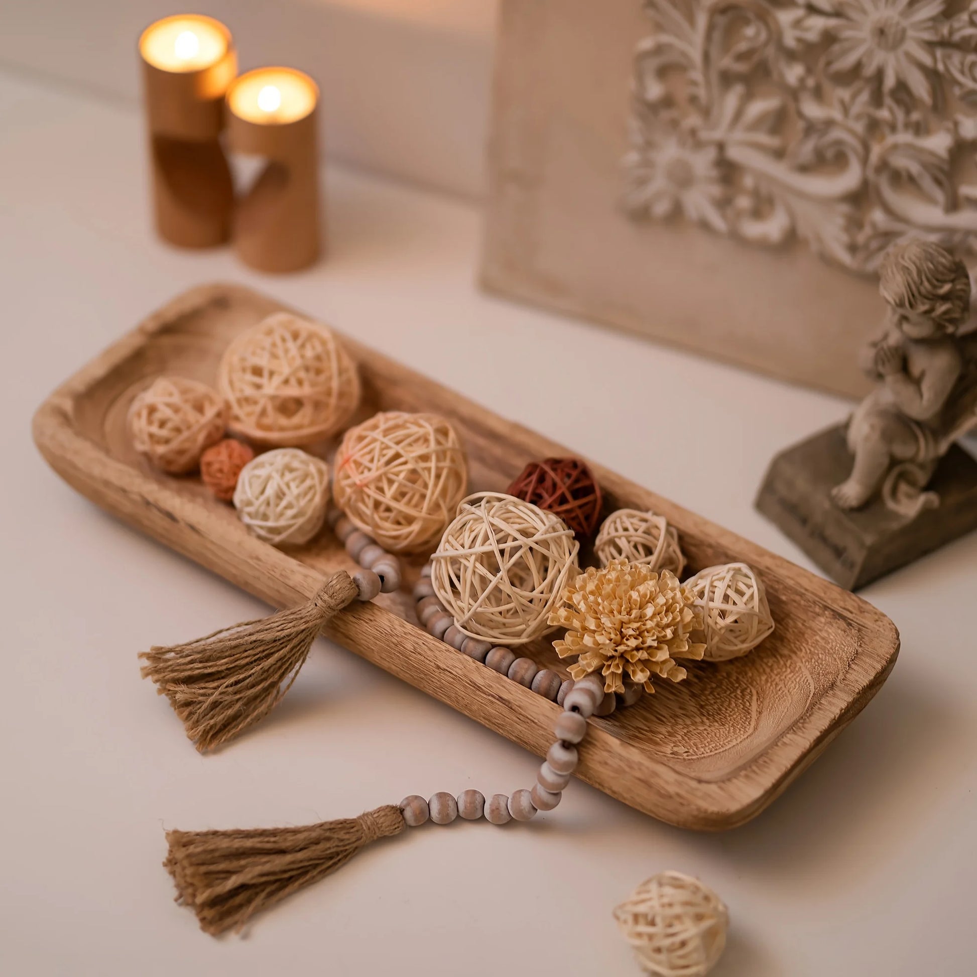 Decorative items including a wooden tray with spherical ornaments and tassels, candles, and a figurine on a neutral background.